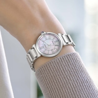 De pols van een vrouw draagt een zilveren horloge met een parelmoeren wijzerplaat.