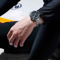 Man in zwart wetsuit met horloge zit op surfplank.