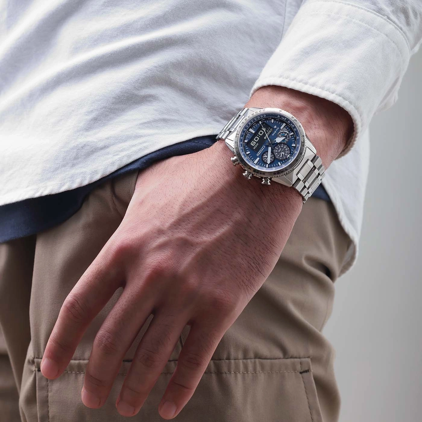 Man draagt zilveren horloge met blauwe wijzerplaat en wit overhemd.