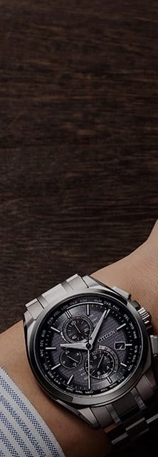 Close-up van een Citizen horloge om een pols, met een donkere houten achtergrond.