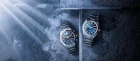 Twee Citizen horloges met blauwe wijzerplaten op een getextureerd oppervlak.