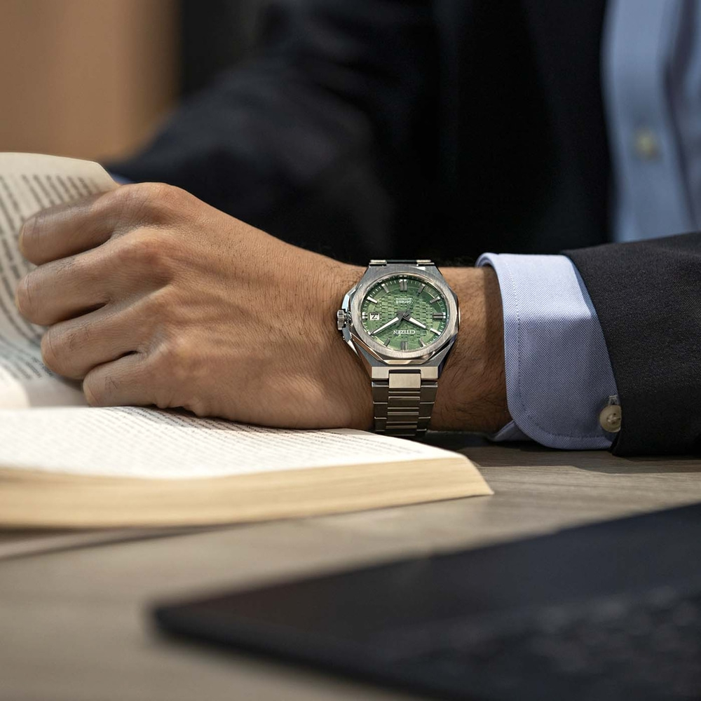 Een man in een pak leest een boek en draagt een groen Citizen horloge.