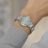 De pols van een vrouw met een zilveren horloge met een lichtgroene wijzerplaat.
