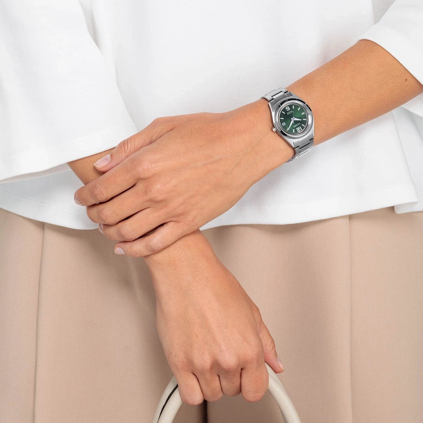 Vrouw met horloge, tas, wit overhemd en beige broek.