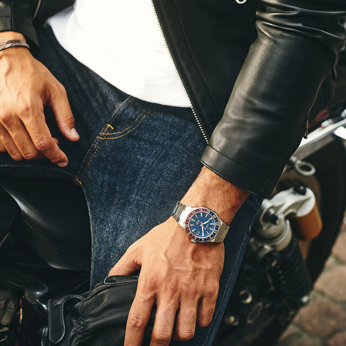 Man met horloge, leren jas en jeans op een motorfiets.