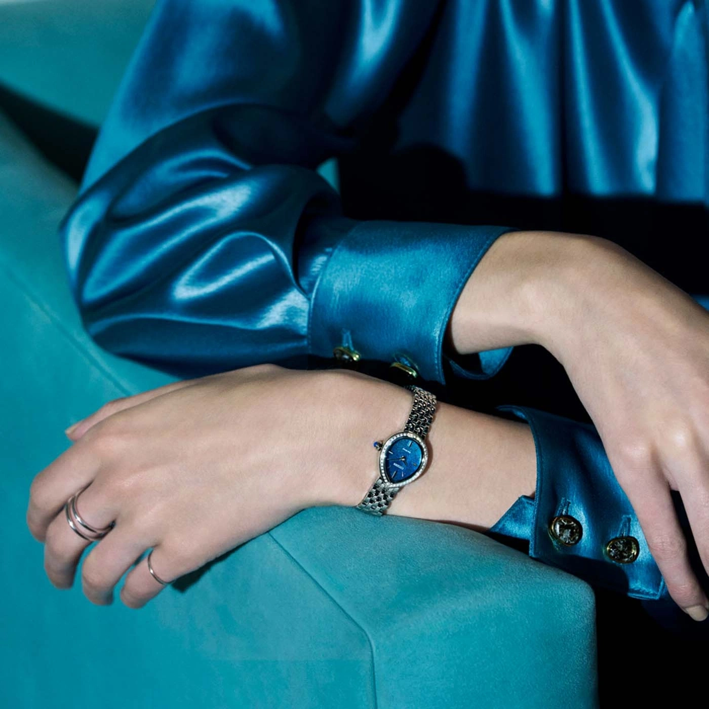 Een vrouw in een blauwe satijnen top en ringen draagt een horloge.