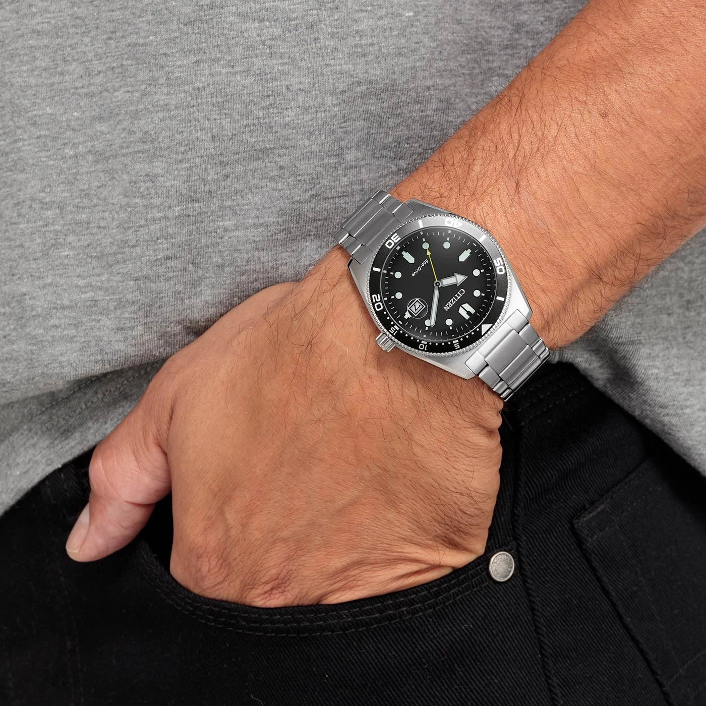 Man met Citizen horloge, hand in zak, zwarte jeans, grijs shirt.