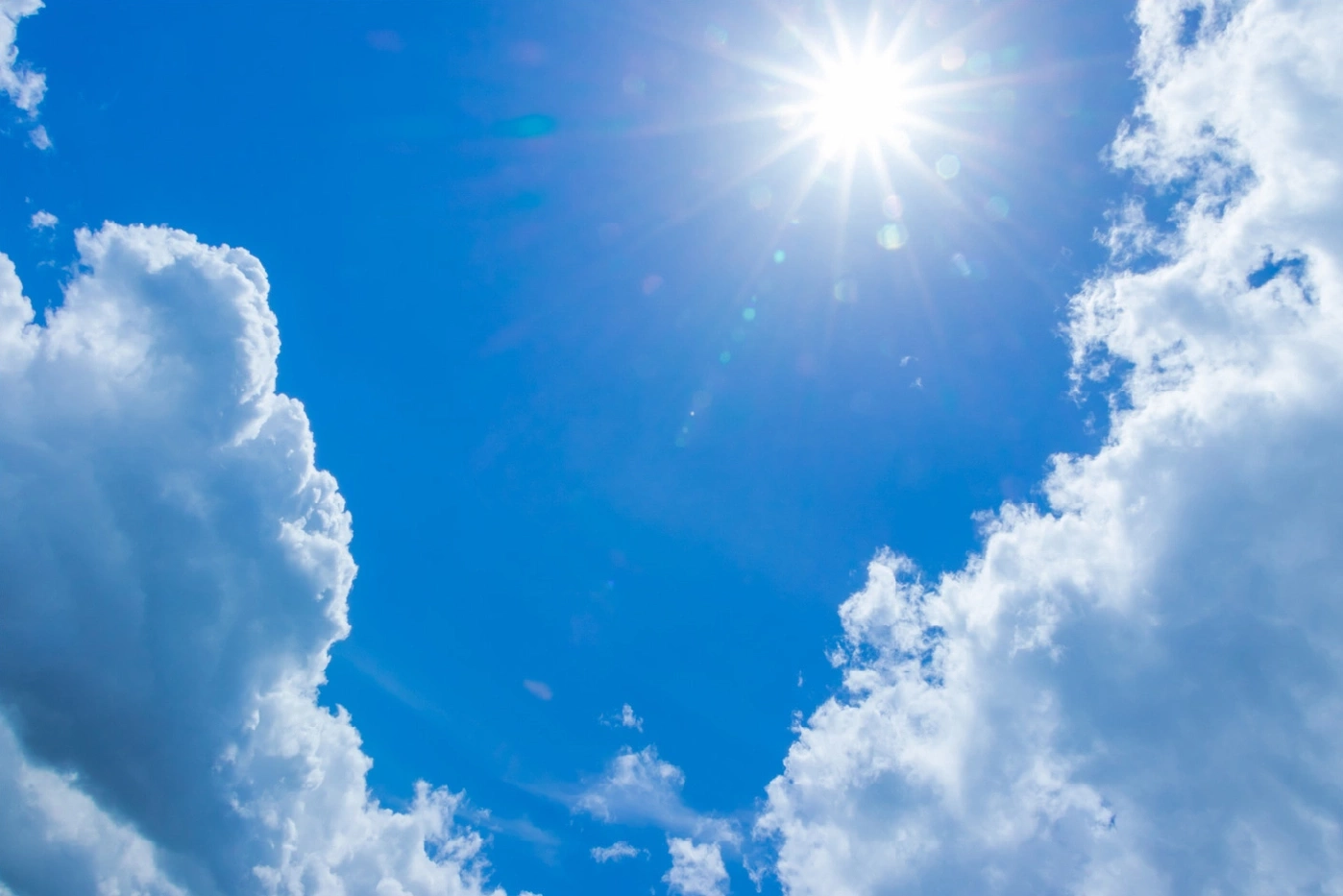 Felle zon schijnt in een heldere blauwe lucht met pluizige witte wolken.