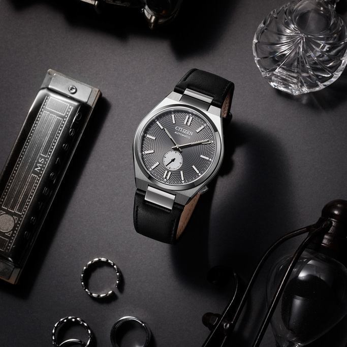 Citizen horloge met zwarte leren band en accessoires op een donkere ondergrond.