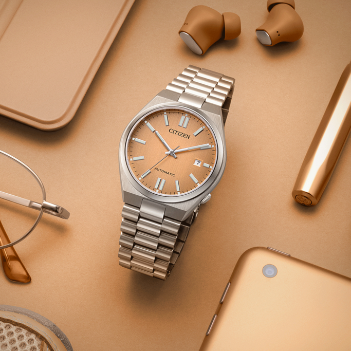 Citizen horloge, oortelefoons, pen, bril en tablet op gouden oppervlak.