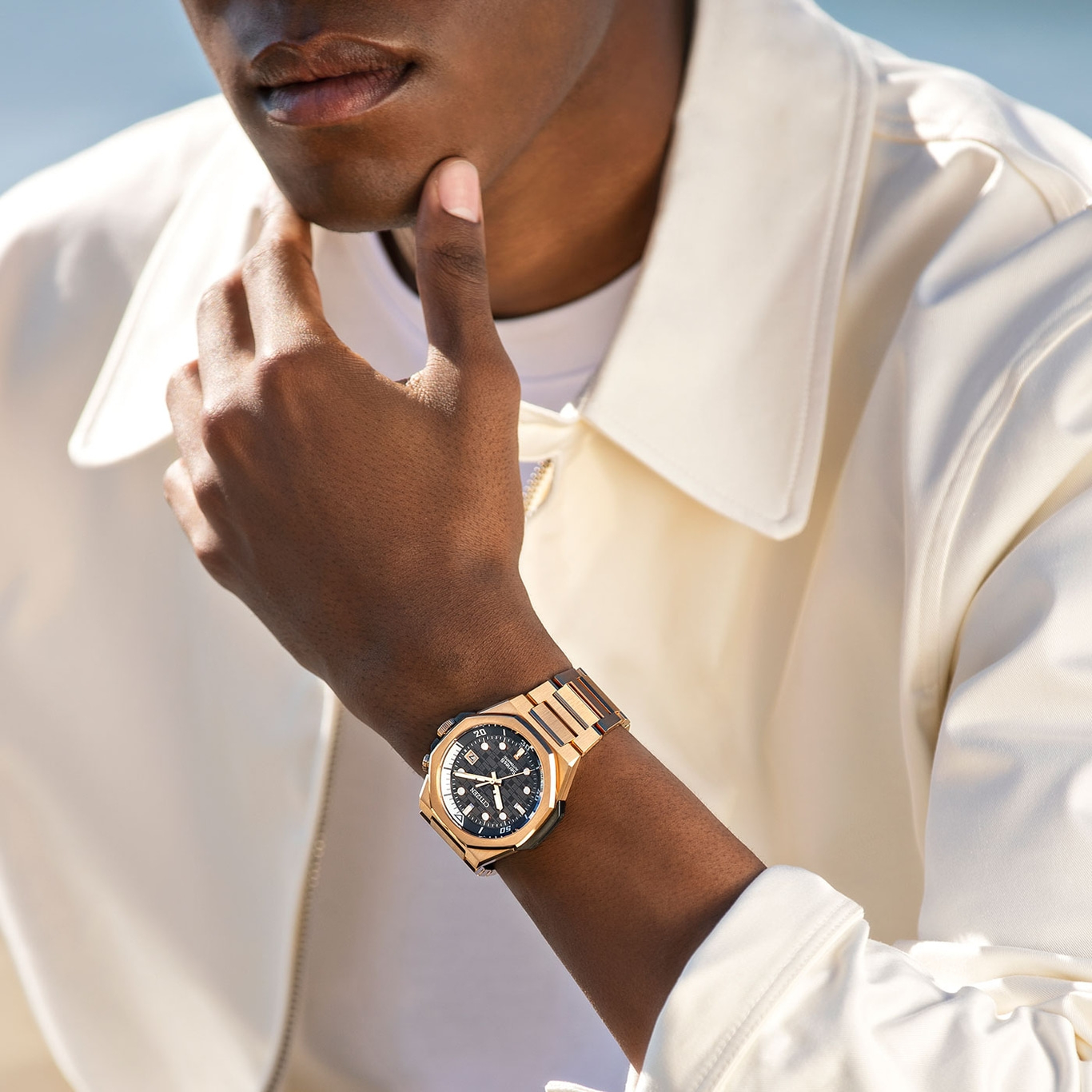 Man met gouden horloge, hand op kin, poseert stijlvol en elegant.