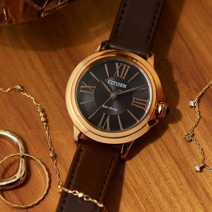 Citizen horloge met bruine leren band en gouden accenten op houten oppervlak met sieraden.