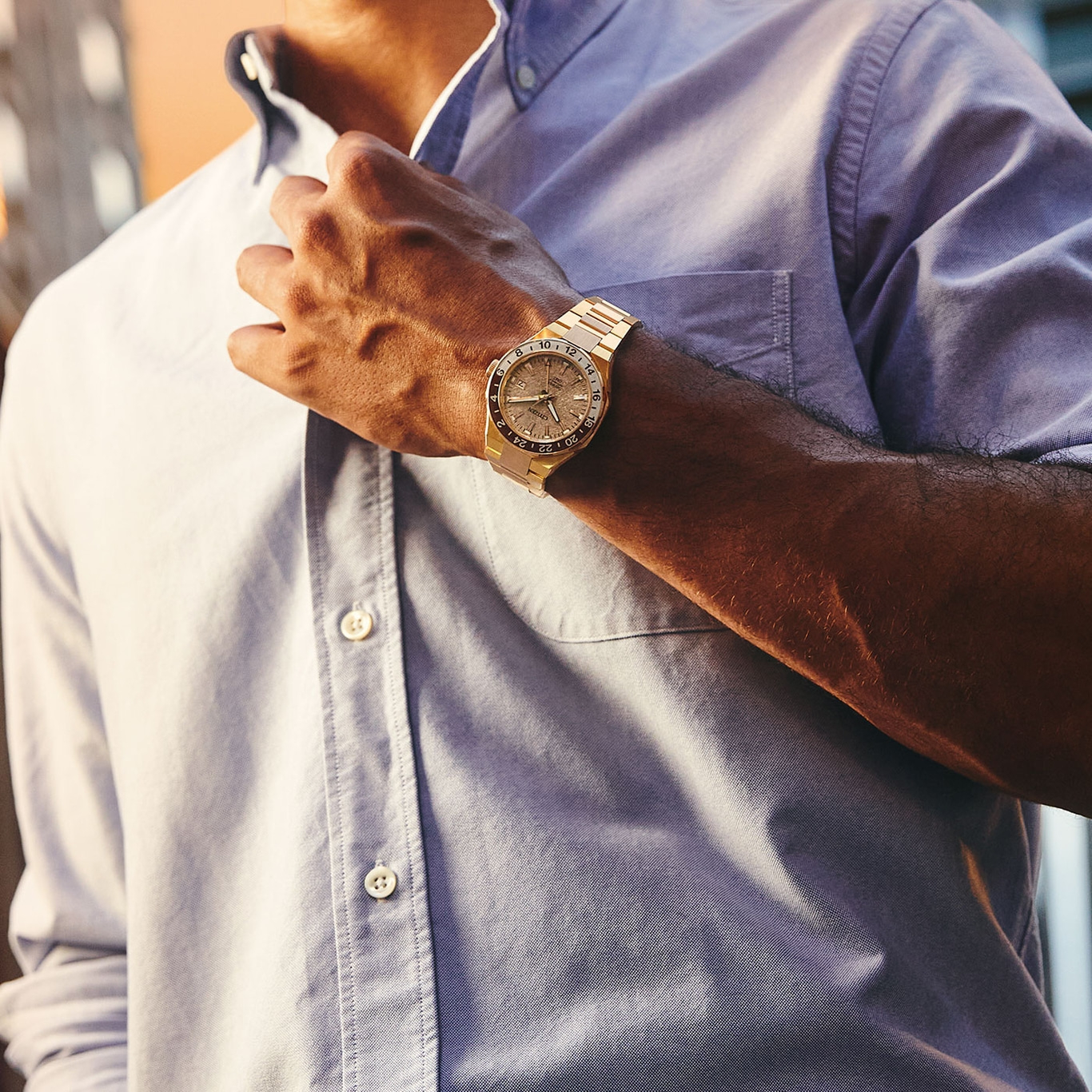 Man met een gouden horloge, knoopt zijn lichtblauwe overhemd dicht.