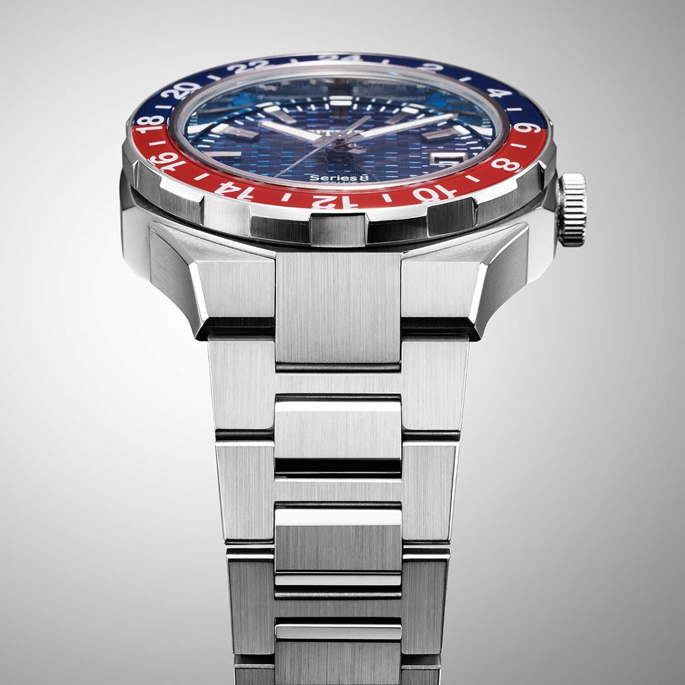 Close-up van een zilveren horloge met een blauw-rode bezel en een metalen band.