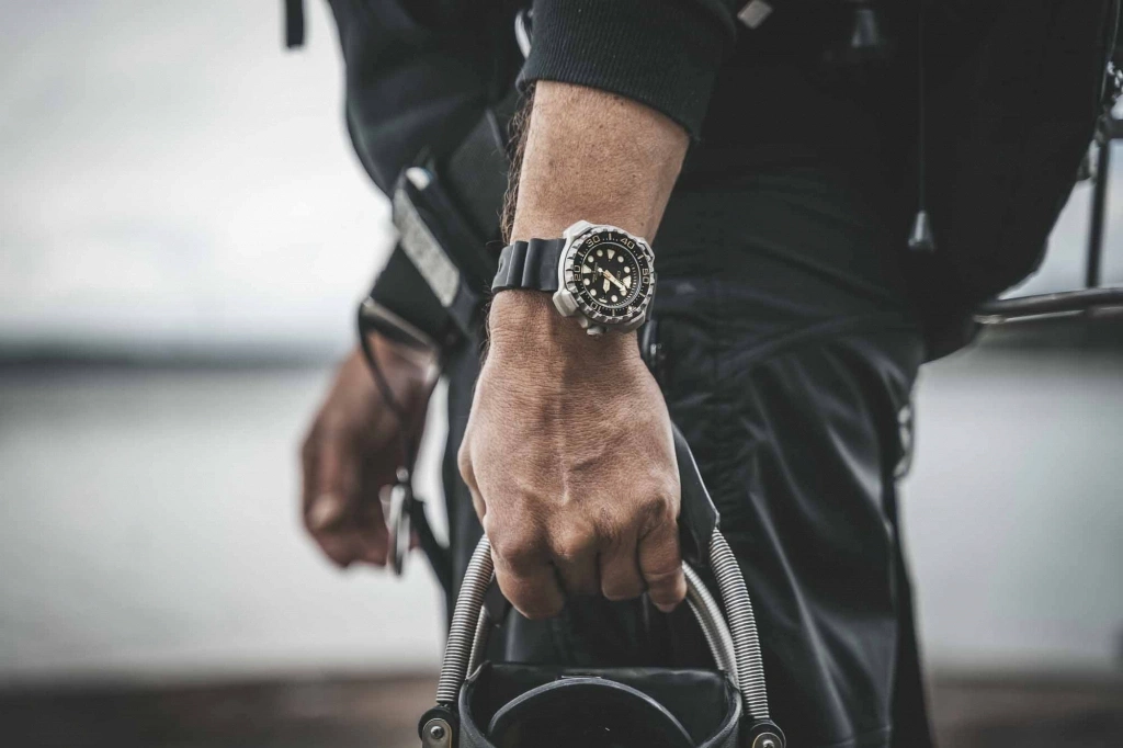 Man met horloge, houdt apparatuur vast, close-up, zwarte outfit, buiten