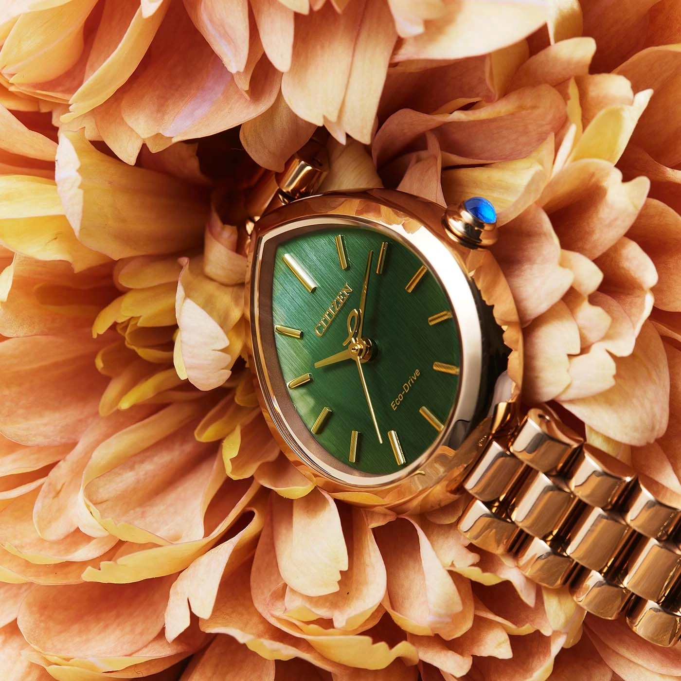 Een gouden horloge met een groen wijzerplaat rust op oranje bloemblaadjes.