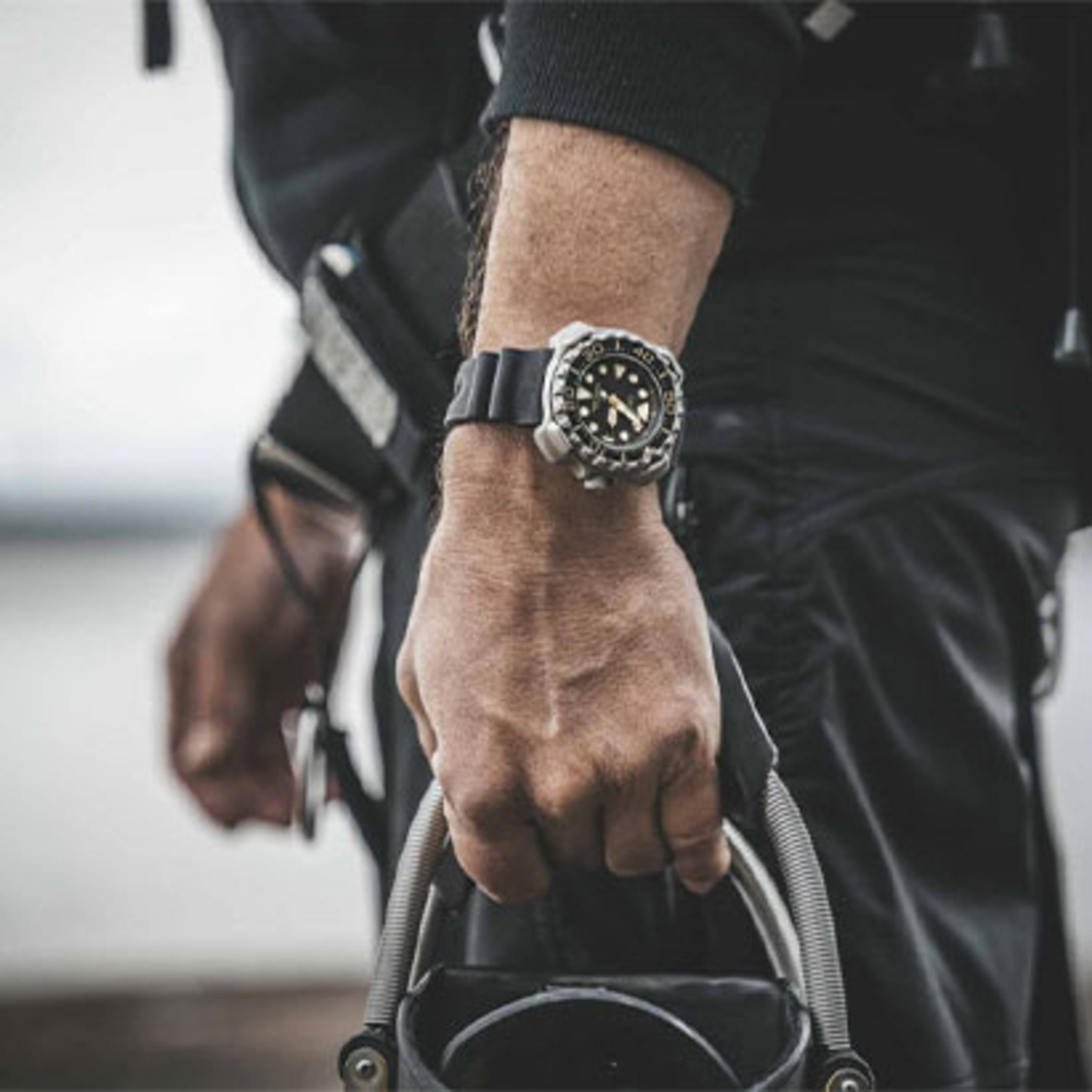 Man met horloge, houdt apparatuur vast, close-up, zwarte outfit, buiten