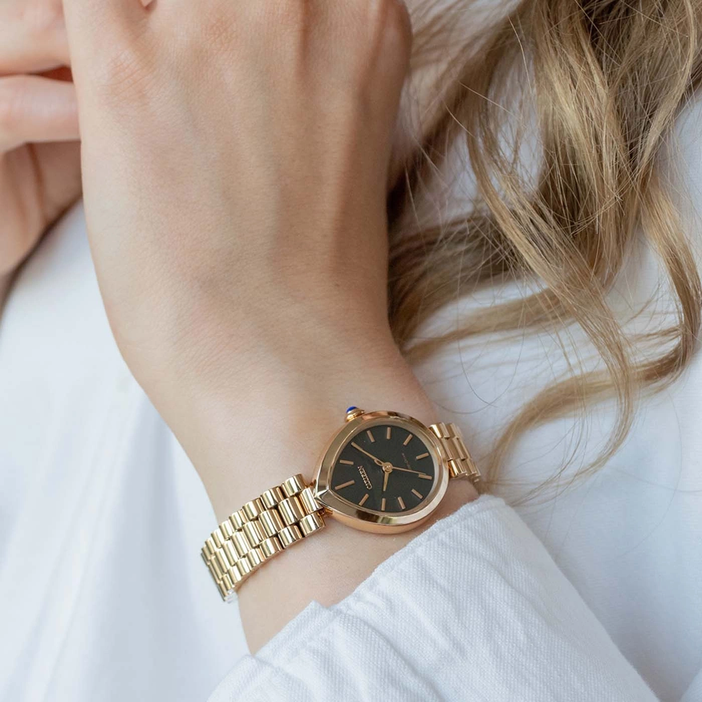 Gouden horloge om de pols van een vrouw tegen een wit overhemd.