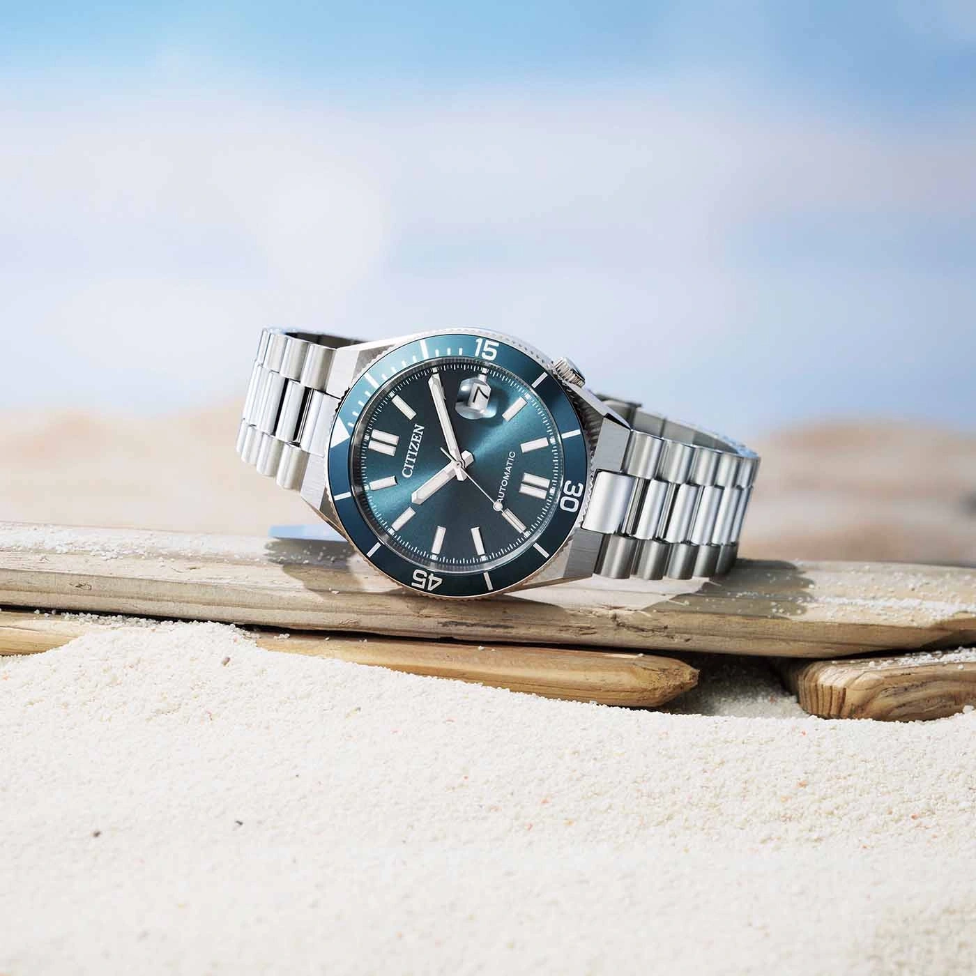 Een Citizen automatisch horloge rust op drijfhout op een zandstrand.
