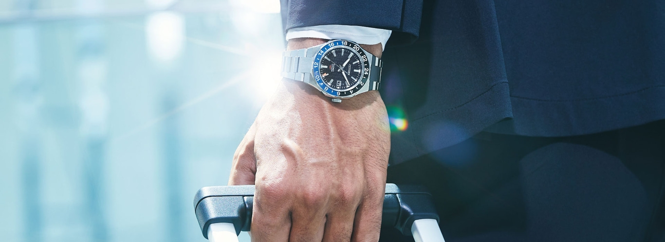 Man met horloge, houdt koffer vast, reist in stijl, zakenreis, elegantie.