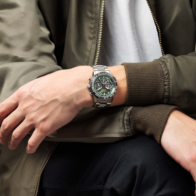 Man met zilveren horloge met groene wijzerplaat en groene jas, close-up.