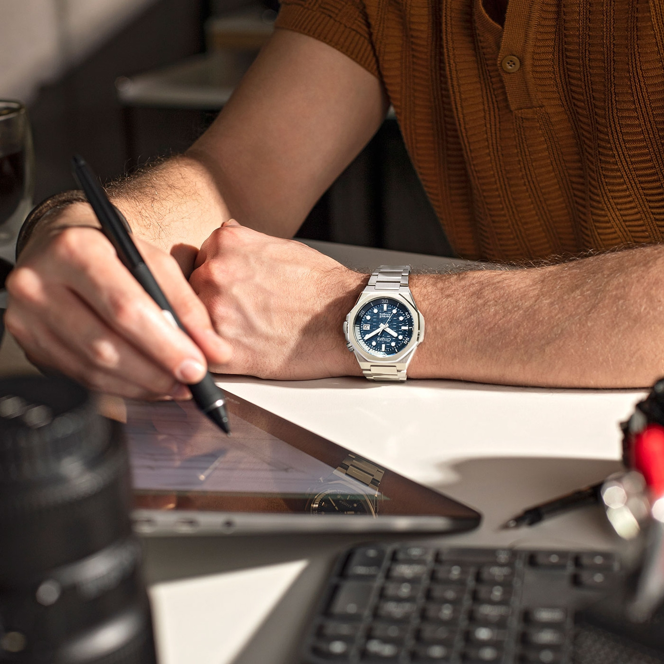 Man werkt op tablet, horloge om pols, pen in de hand.