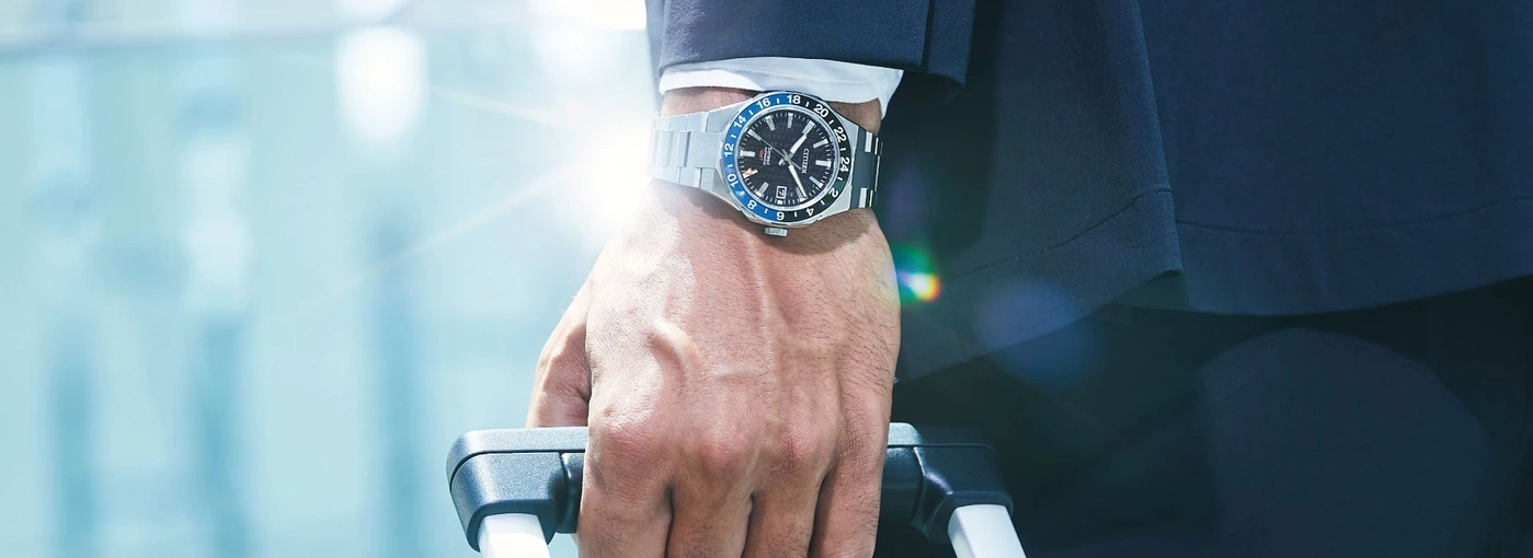 Man met horloge, houdt koffer vast, reist in stijl, zakenreis, elegantie.