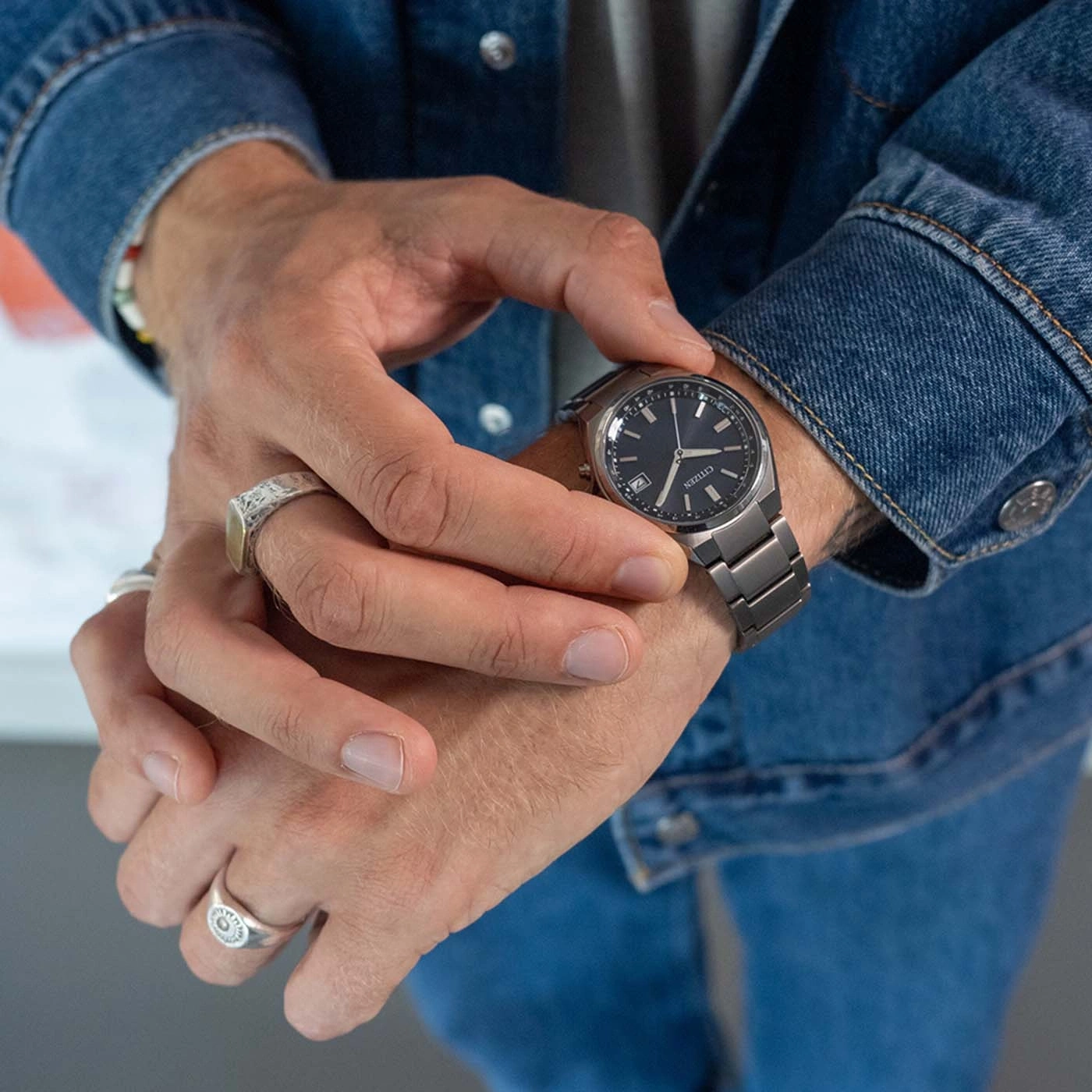 Man controleert zijn horloge, draagt een spijkerjack en ringen.
