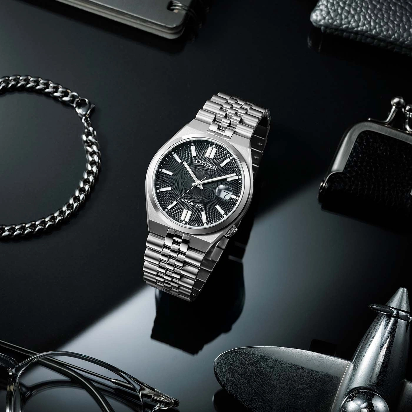 Citizen horloge op reflecterend oppervlak met accessoires, zwarte achtergrond.