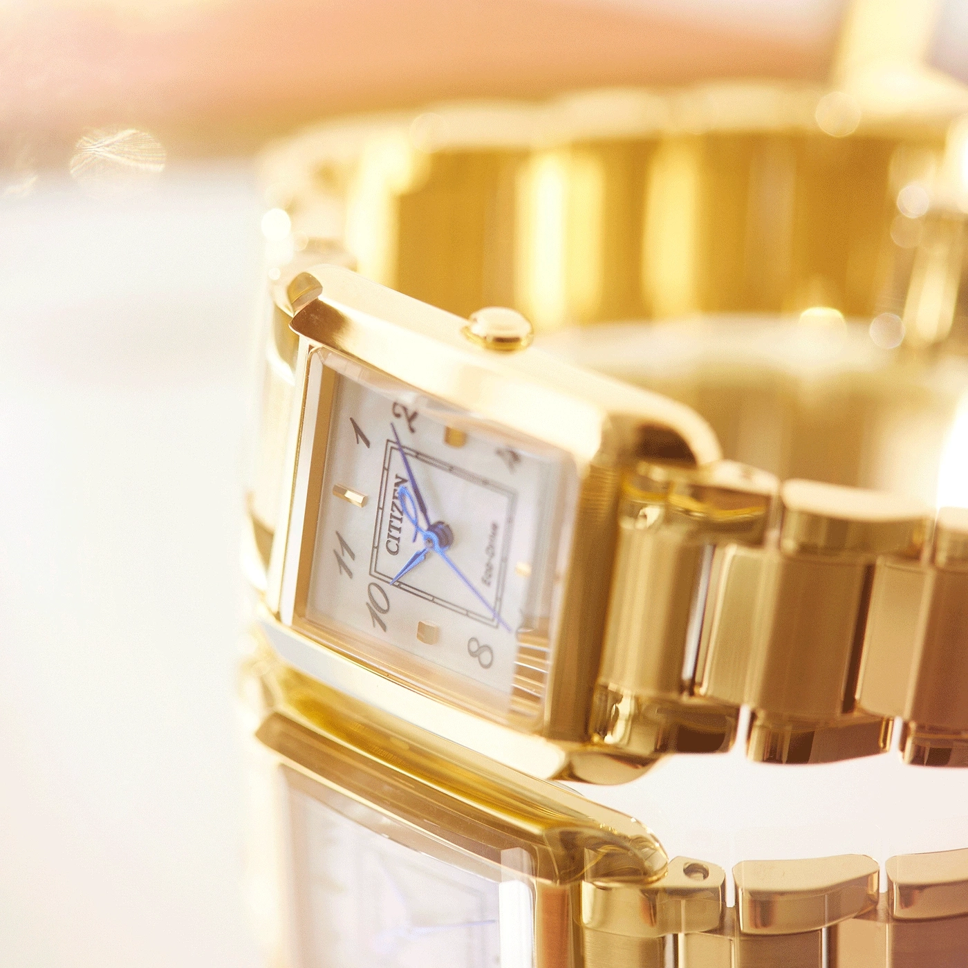 Close-up van een gouden Citizen horloge met een rechthoekige wijzerplaat en blauwe wijzers.