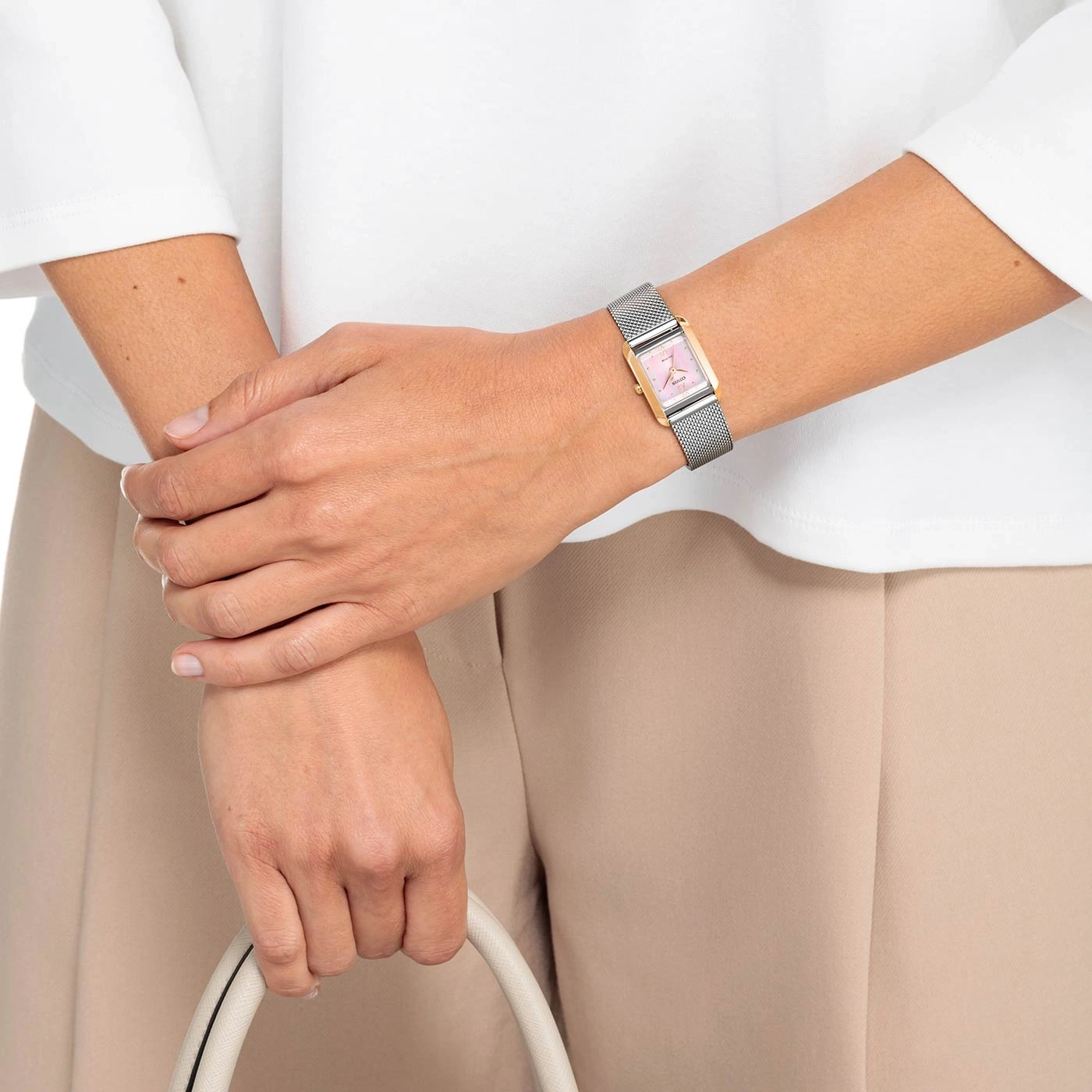 Vrouw met horloge, tas, wit overhemd en beige broek.