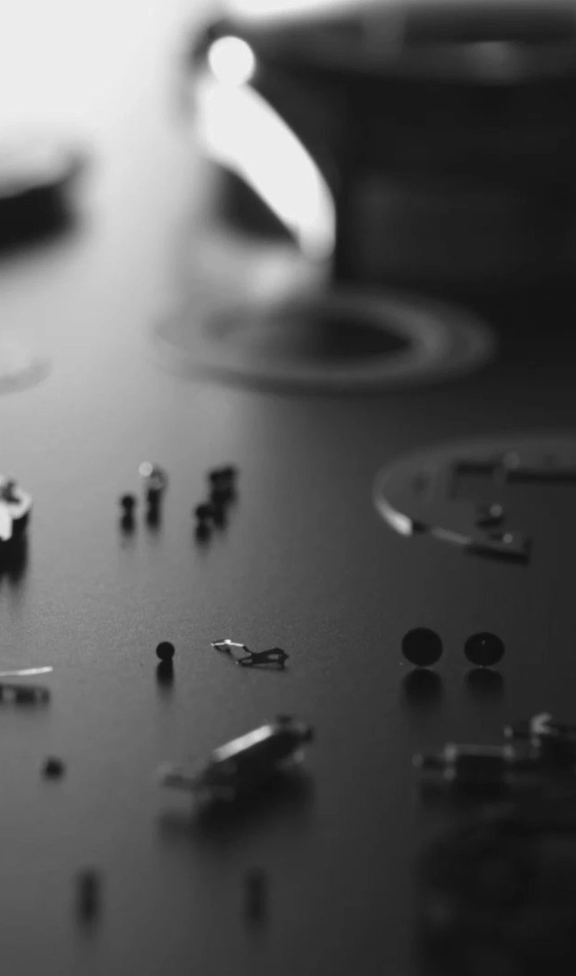 Horloge onderdelen verspreid op een donker oppervlak, monochroom, close-up.