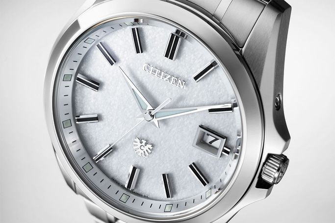 Close-up van een zilveren Citizen horloge met een getextureerde witte wijzerplaat en datumweergave.