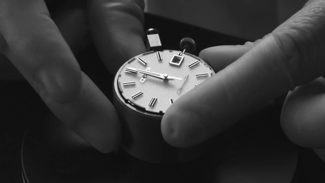 Close-up van een horloge dat door twee handen wordt vastgehouden, wijzerplaat zichtbaar.