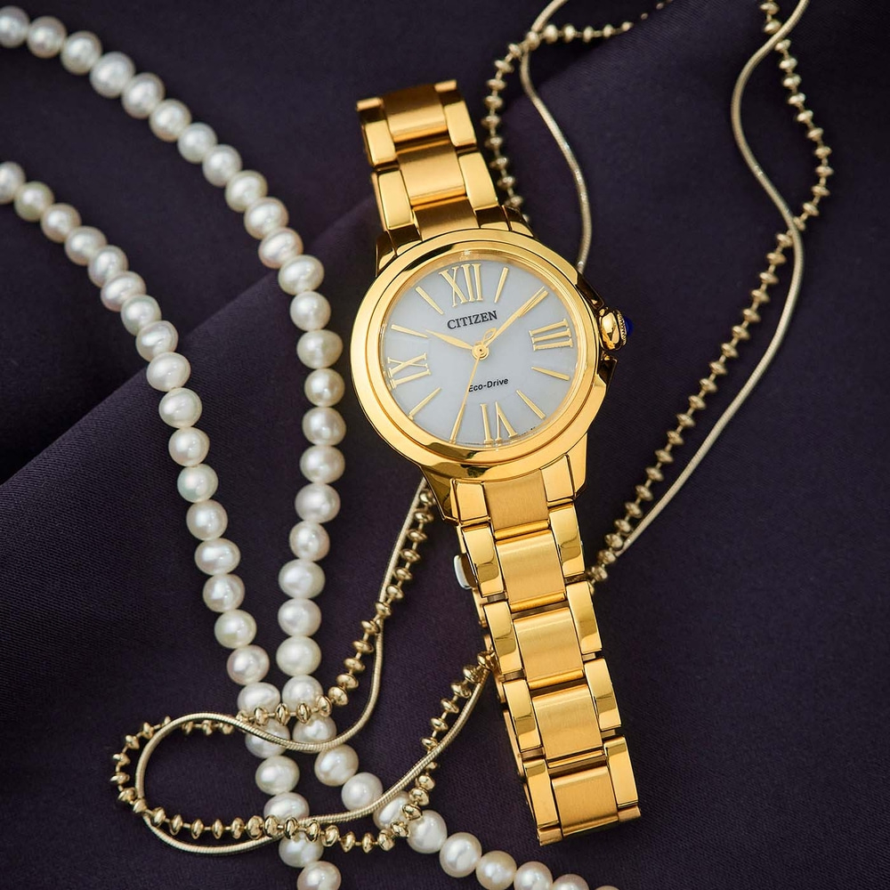 Gouden horloge met parelketting op donkere stof