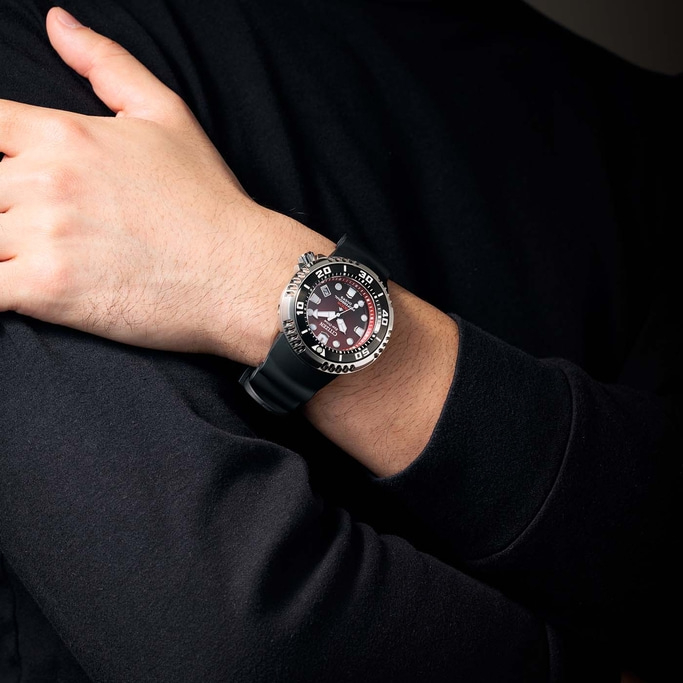 Man draagt Citizen horloge met zwarte band en rode wijzerplaat.