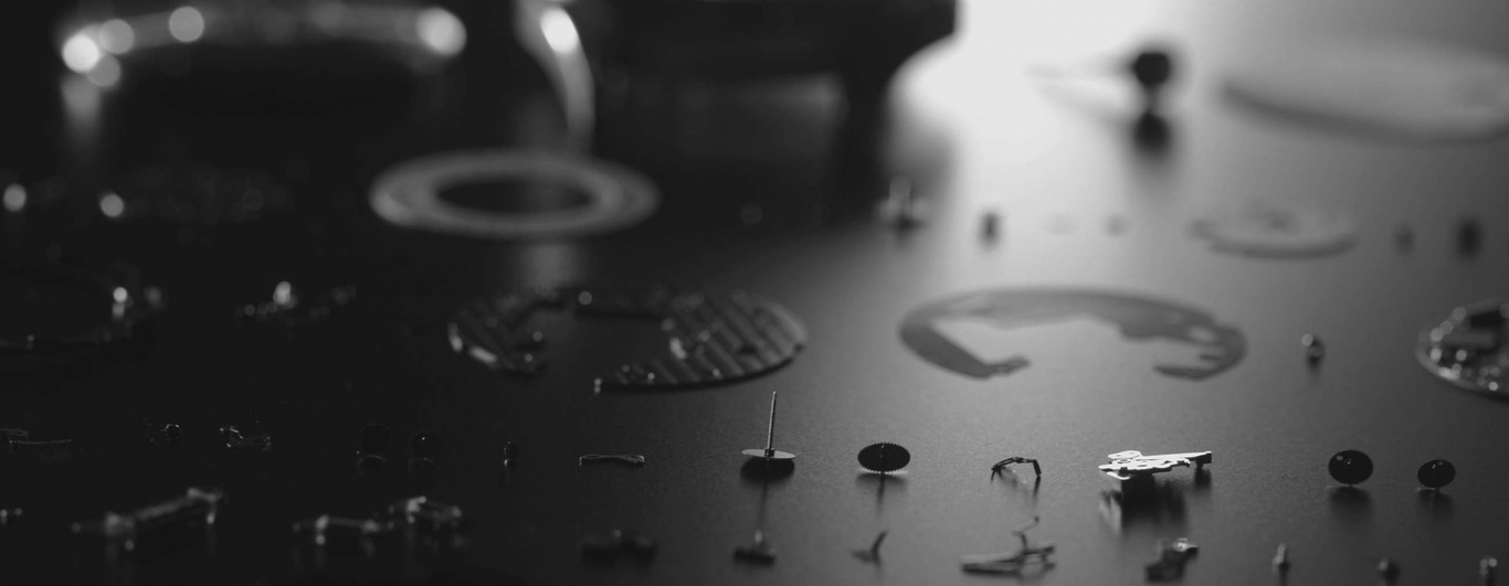 Zerlegte Uhrteile auf dunkler Oberfläche, zur Reparatur oder Wartung auseinandergenommen.