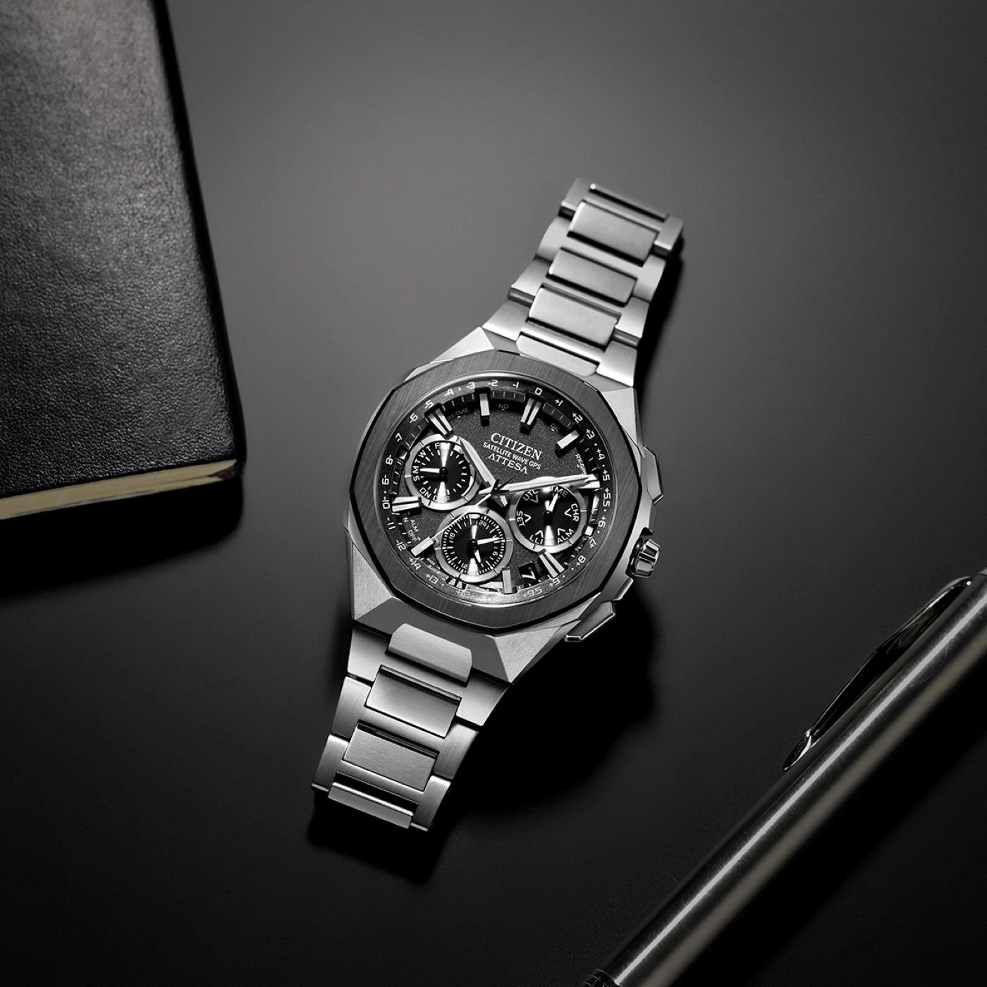 Citizen horloge op een zwart oppervlak met een pen en notitieboek.